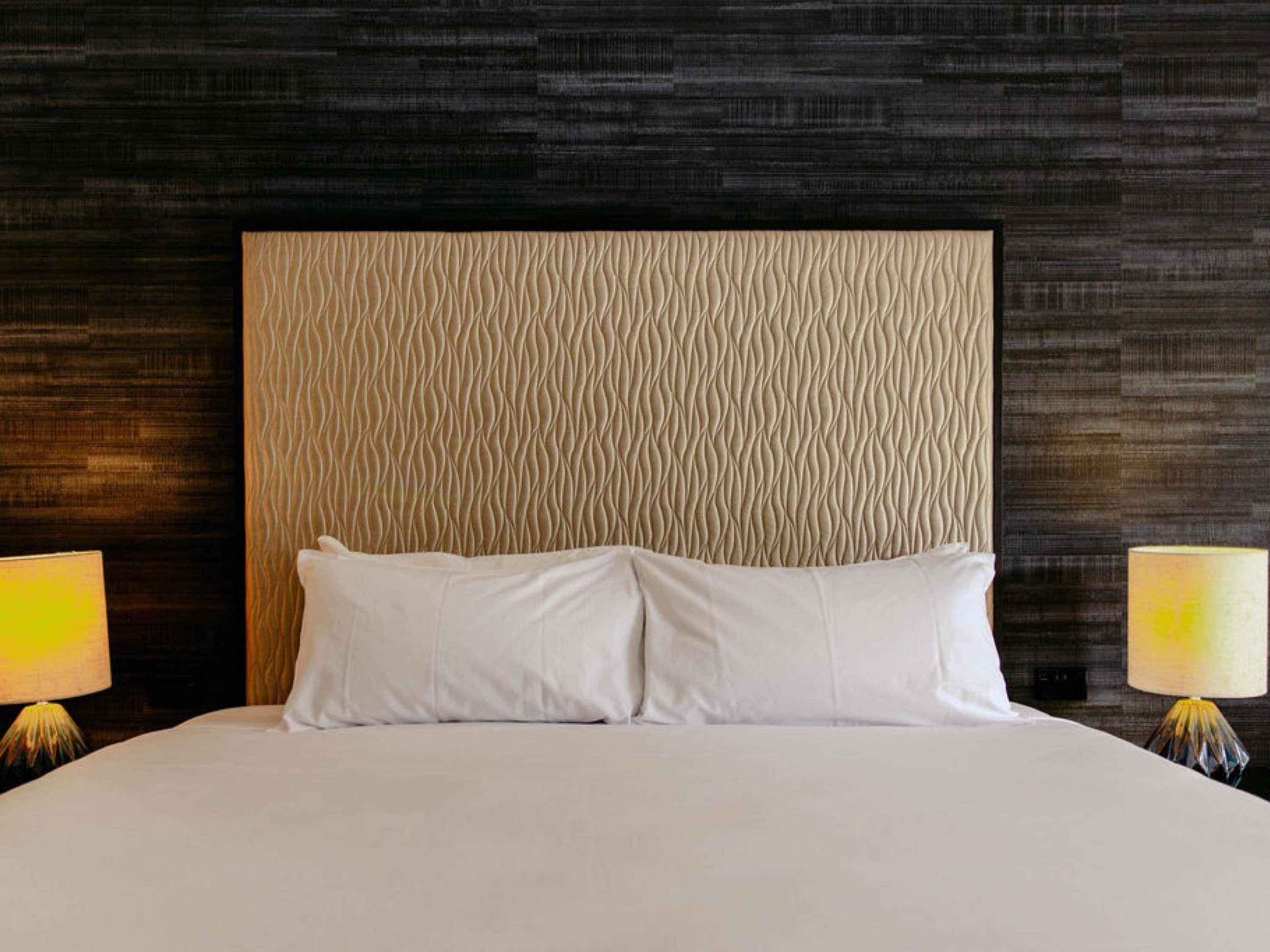 A hotel room with a large bed, two bedside lamps, and a textured headboard.