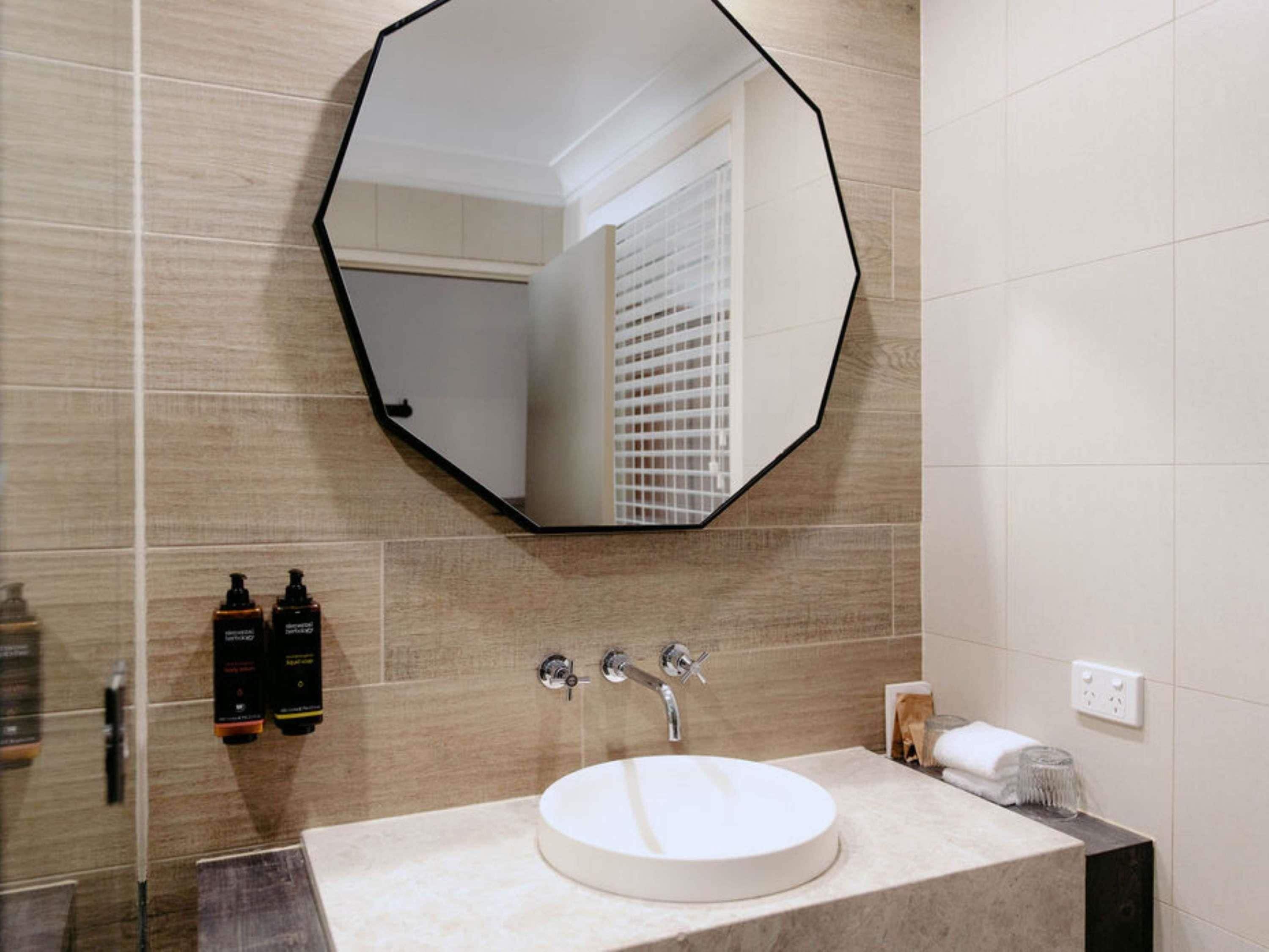 Un baño con un lavamanos redondo, un espejo octogonal grande y un perchero para toallas.