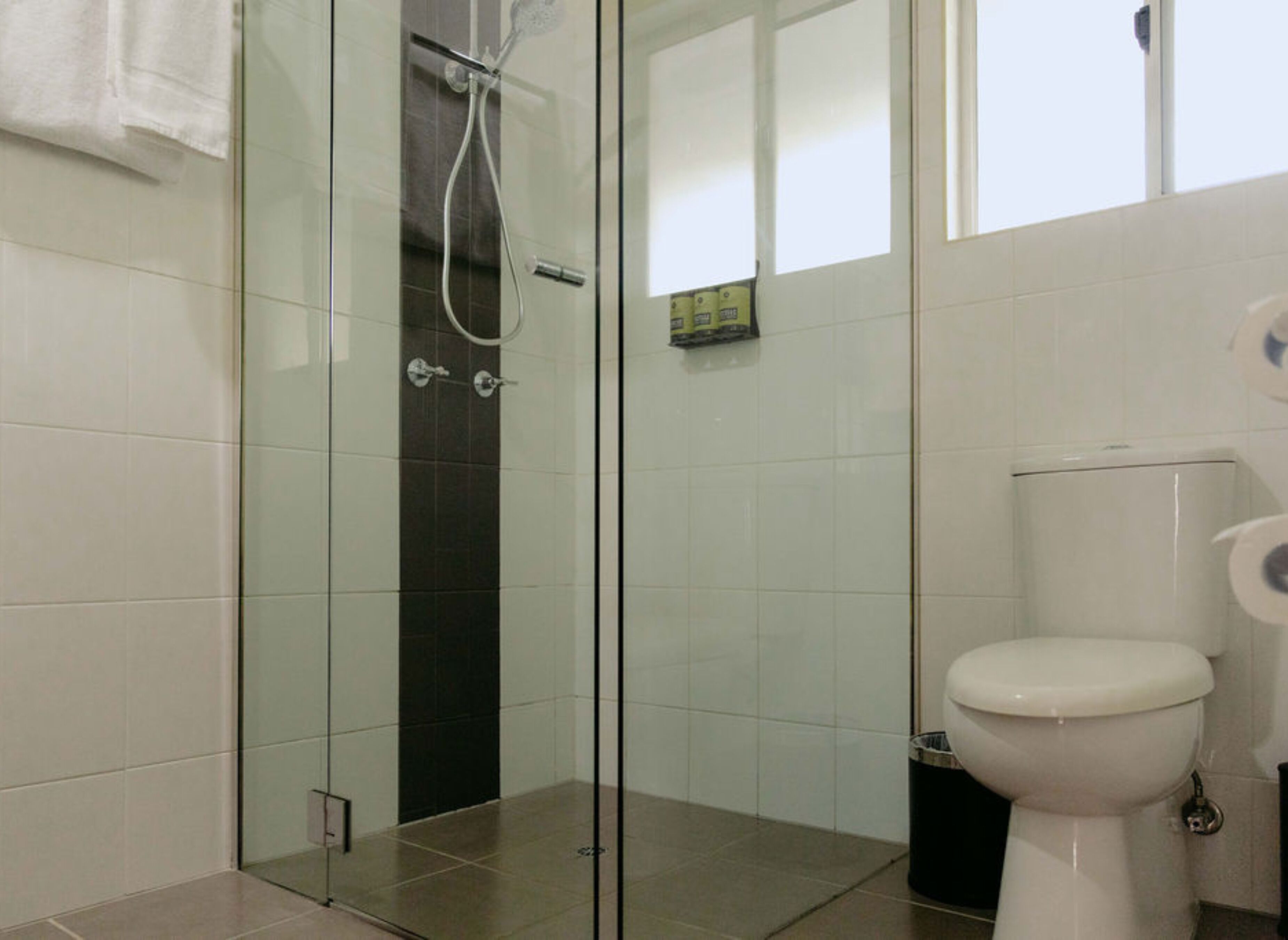 A bathroom with a glass-enclosed shower, a toilet, and a trash bin.