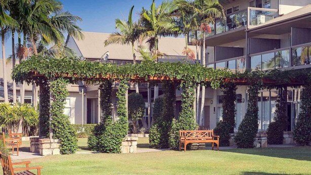 A courtyard with a pergola covered in greenery, a wooden bench, and a palm tree. - Mercure Clear Mountain Lodge (Cashmere)