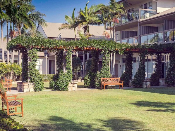 A courtyard with a pergola covered in greenery, a wooden bench, and a palm tree. - Mercure Clear Mountain Lodge (Cashmere)