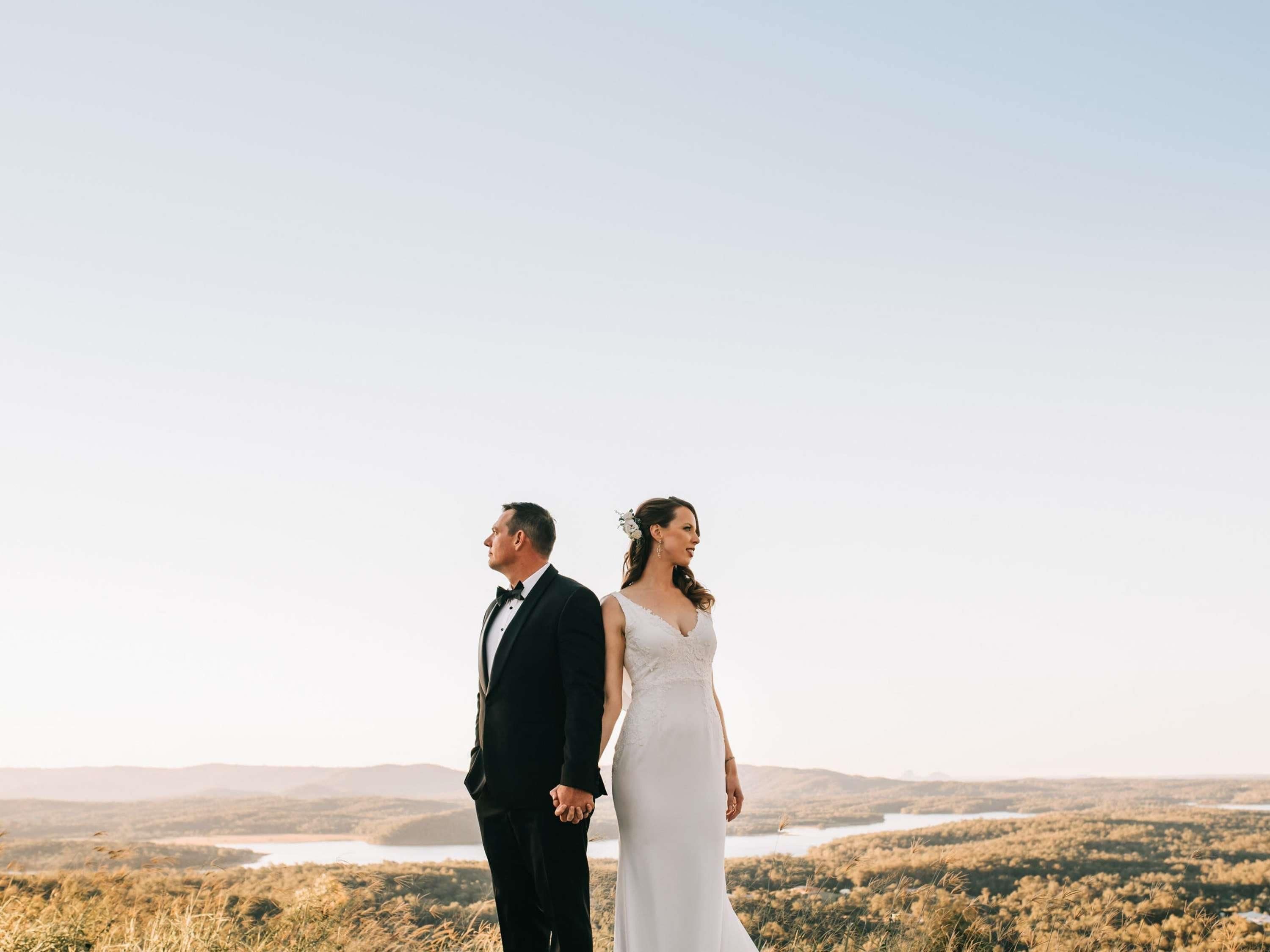 Una pareja está de pie en una colina con vista a un lago y más colinas.