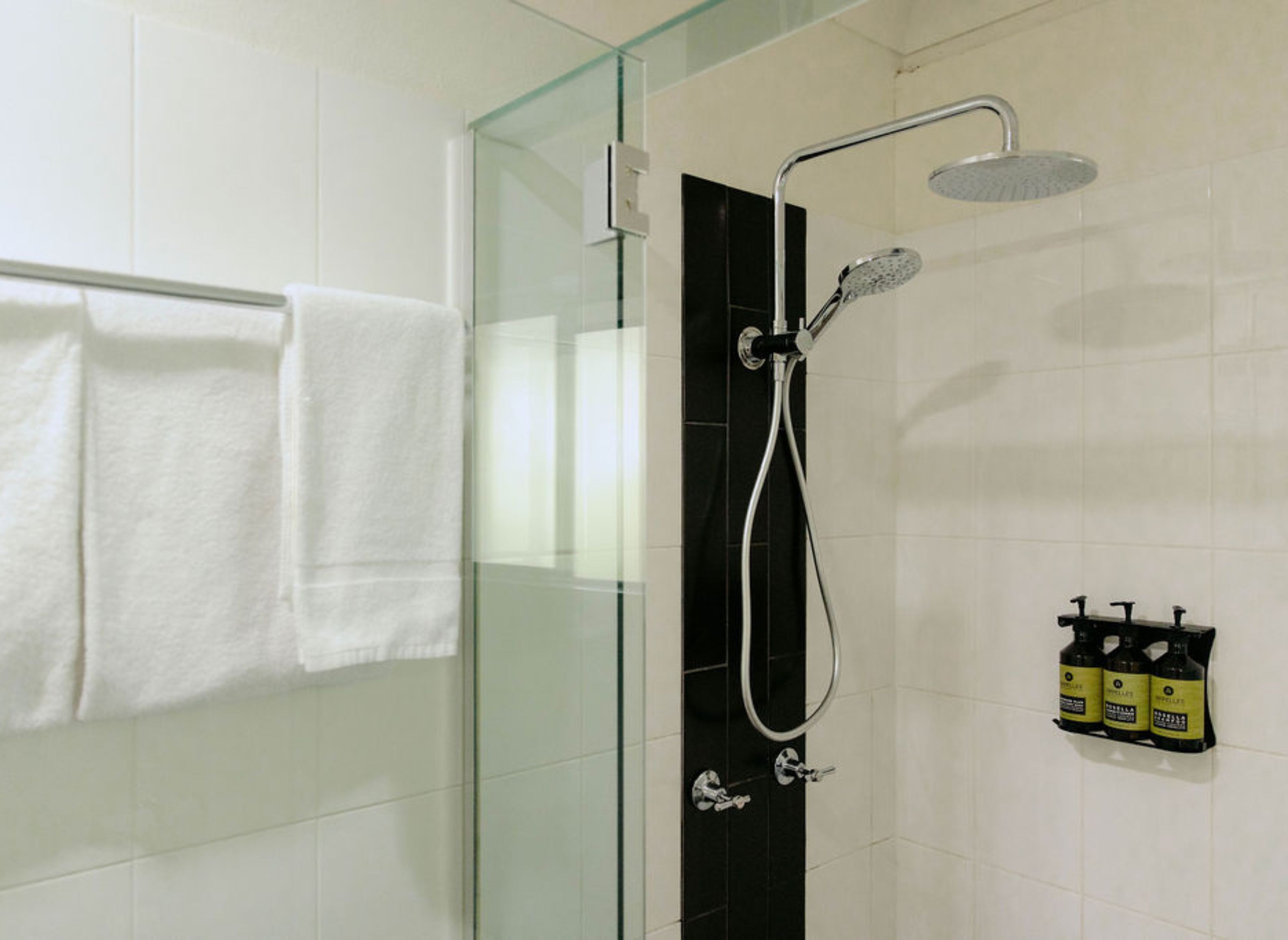 A glass-enclosed shower with a handheld showerhead and a wall-mounted faucet.