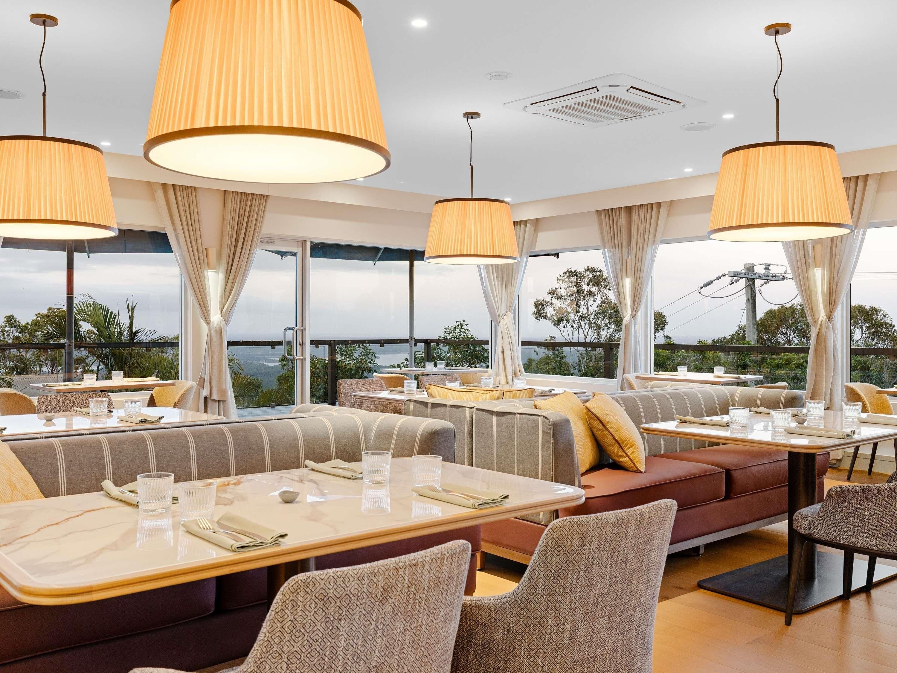 A restaurant with high tables and cushioned seating, large pendant lights, and a view of the landscape.