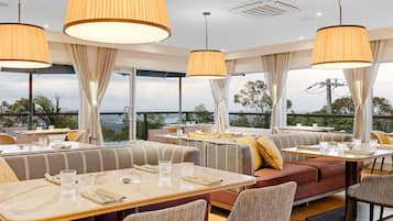 A restaurant with high tables and cushioned seating, large pendant lights, and a view of the landscape.