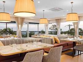 Un restaurante con mesas altas, asientos acolchados, grandes lámparas colgantes y vistas al paisaje.