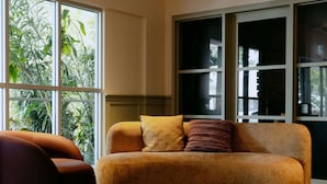 Una habitación con sofá, una silla y un ventanal con plantas visibles afuera.