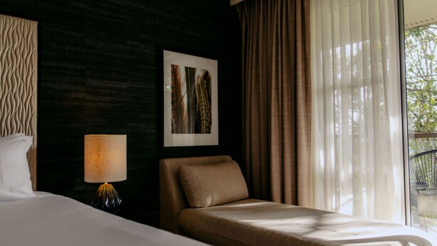 Habitación de hotel con cama, mesita de noche con lámpara, un cuadro en la pared y vista por la ventana.