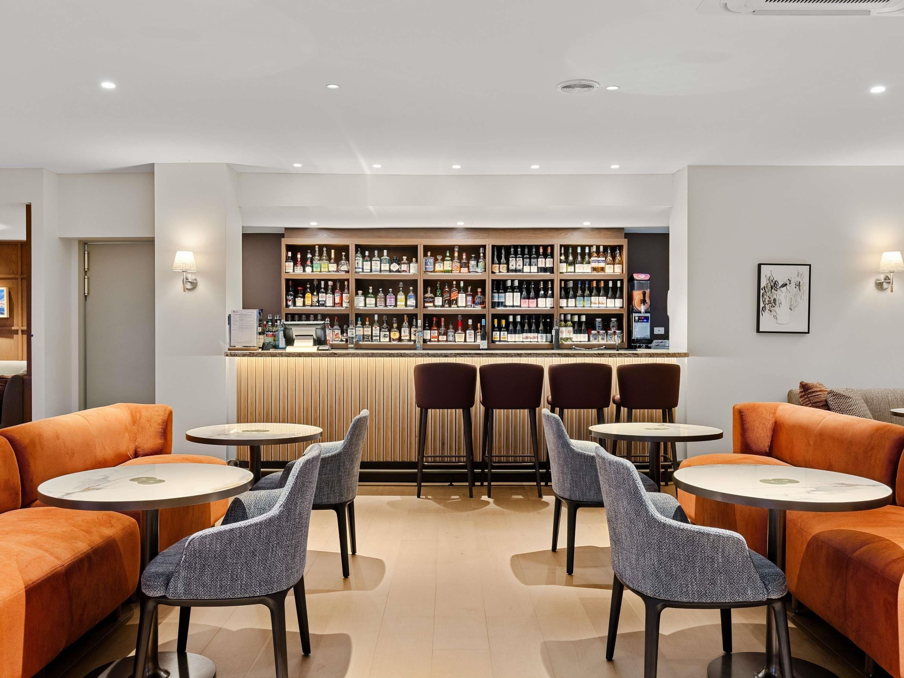 A bar area with multiple shelves of bottles, bar stools, and tables.