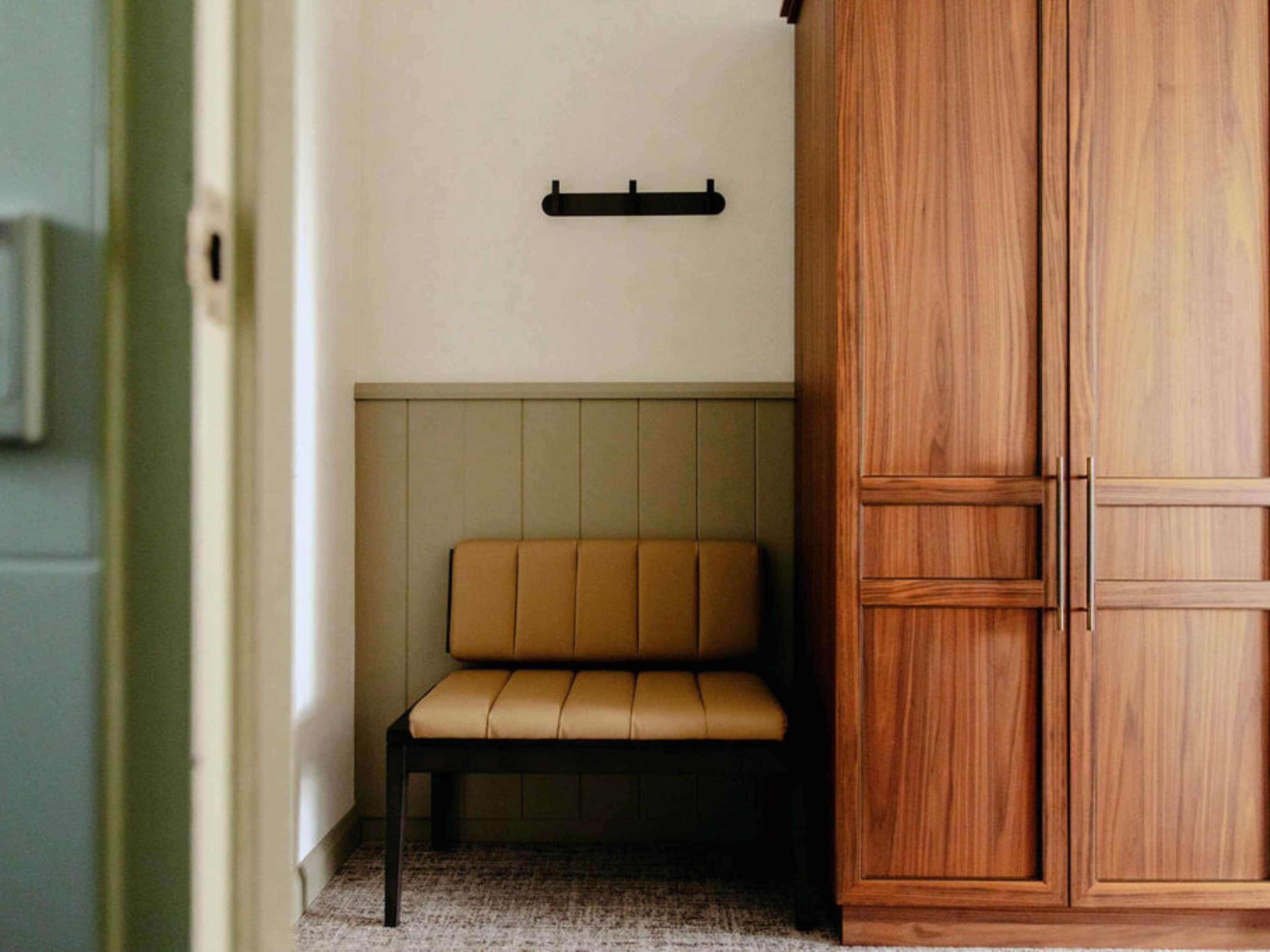 A room with a bench, a wooden wardrobe, and a wall-mounted shelf.