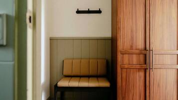 A room with a bench, a wooden wardrobe, and a wall-mounted shelf.