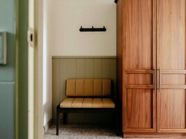 Una habitación con un banco, un armario de madera y un estante en la pared.