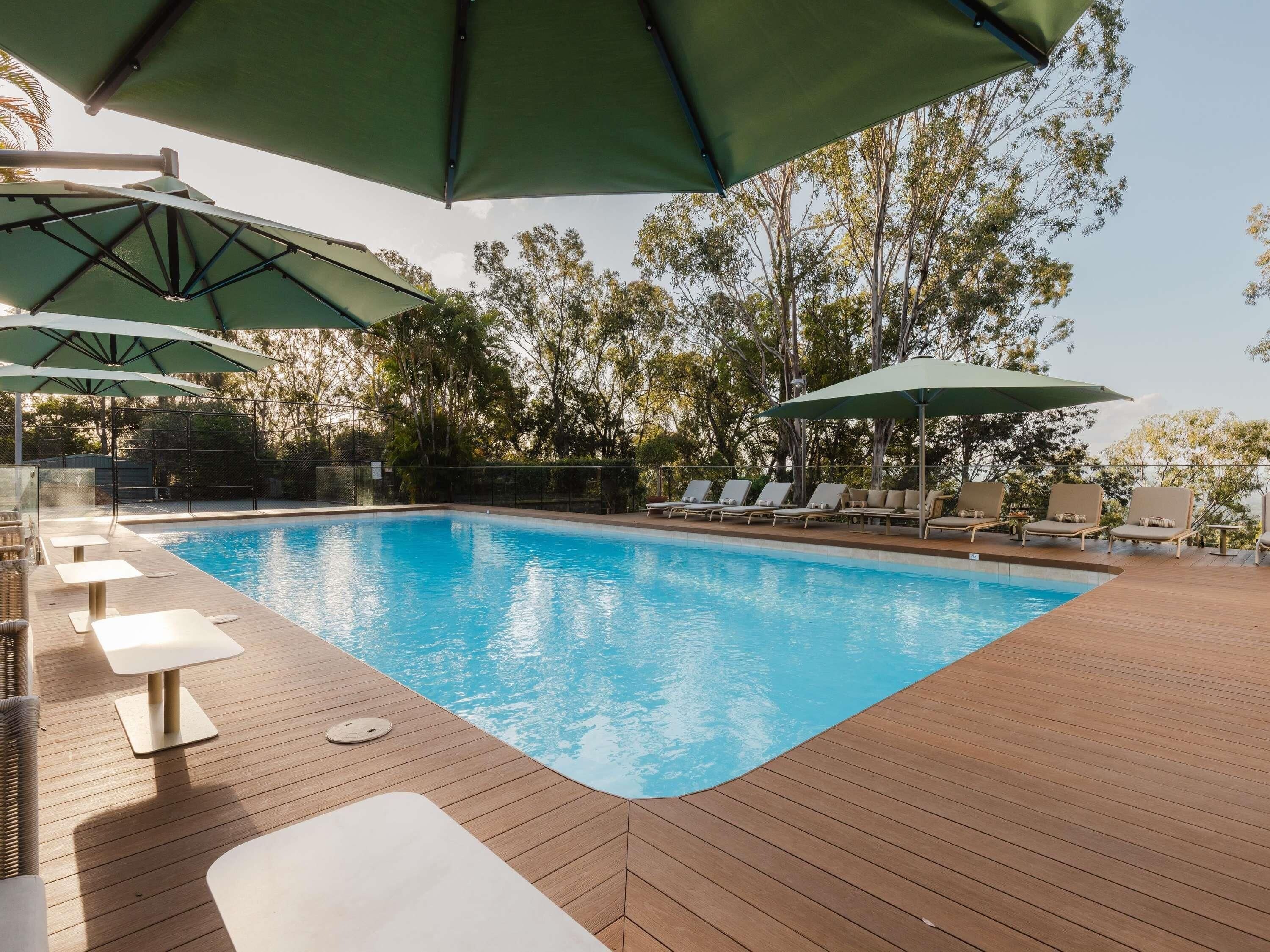 A swimming pool with lounge chairs and umbrellas, surrounded by trees.
