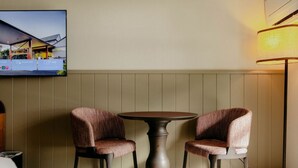 Una habitación con una mesa redonda y dos sillas, un televisor montado en la pared y una lámpara de pie.