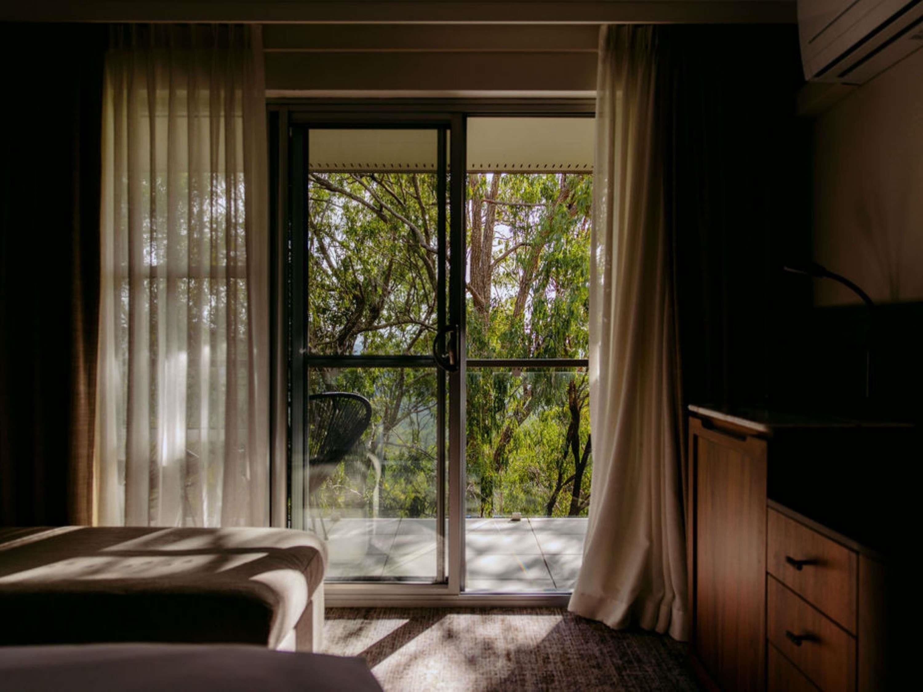Una habitación con una cama, un armario de madera y vistas a un espacio exterior con árboles a través de un ventanal.