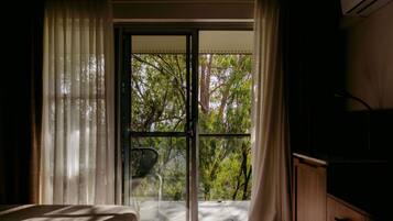 Una habitación con una cama, un armario de madera y vistas a un espacio exterior con árboles a través de un ventanal.
