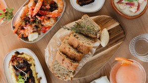 Variedad de platos que incluyen mariscos, pan y una bebida, dispuestos sobre una mesa de madera.