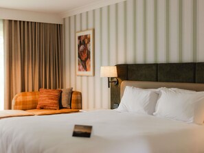 A hotel room with a large bed, a headboard, a nightstand, a lamp, a window with curtains, and a wall with a striped pattern. - Peppers Clear Mountain (Cashmere)