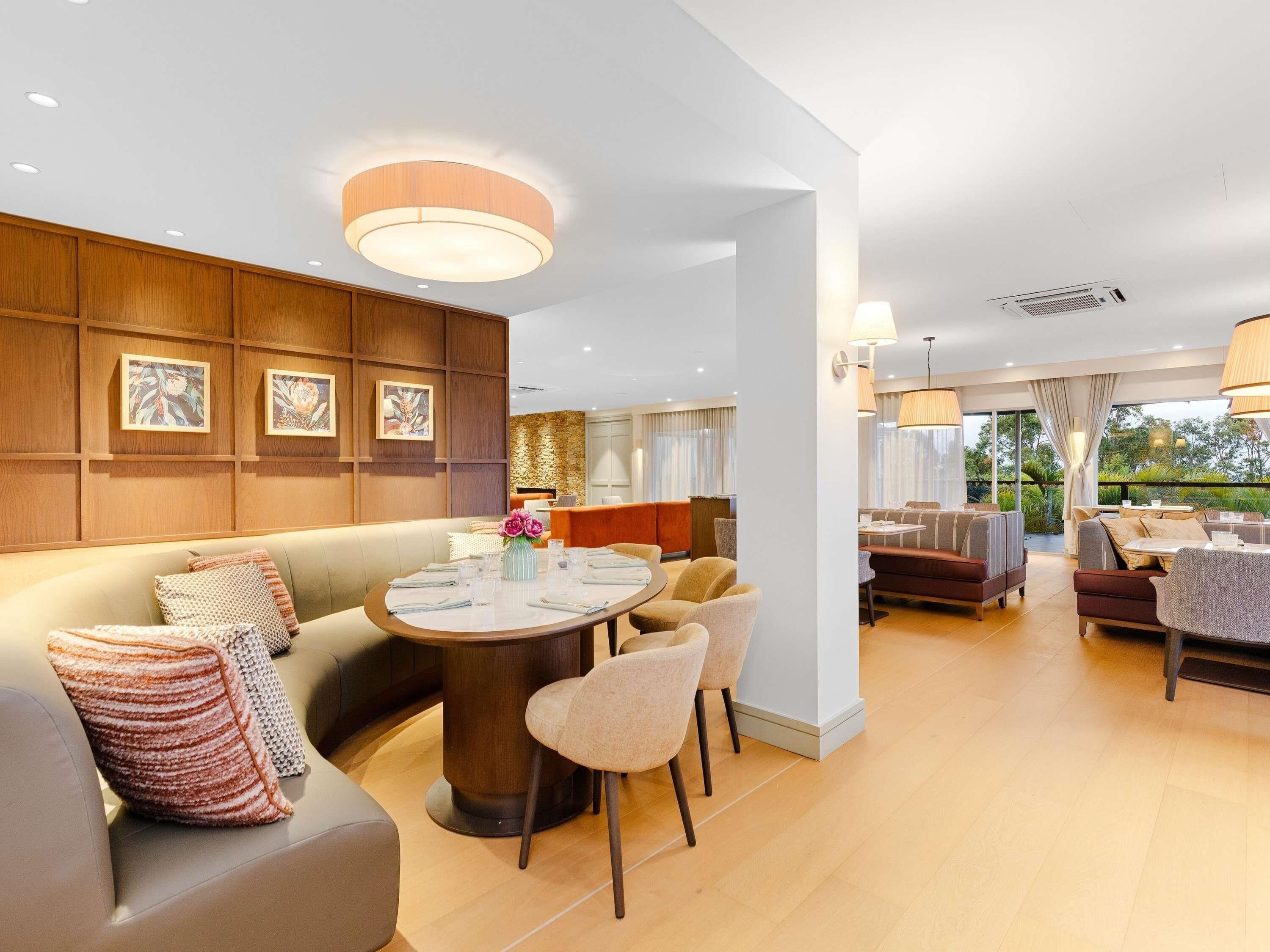 A modern hotel room with a dining area, a sofa, and a view of the outdoors.