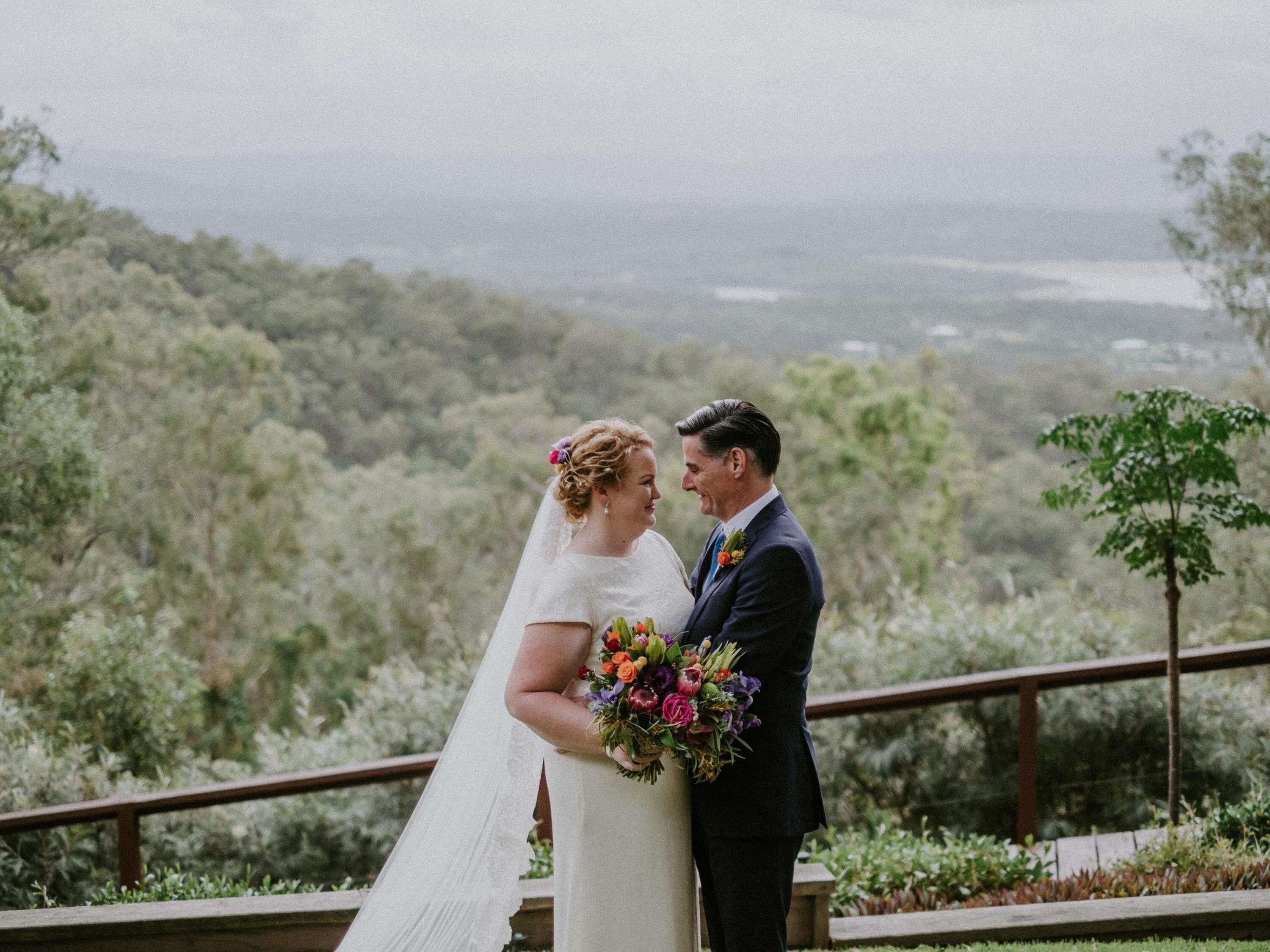 Una pareja parada en un balcón con vistas a un paisaje boscoso.