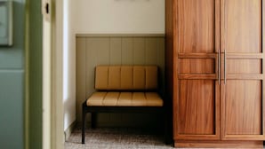 Una habitación con un armario de madera, un banco y una estantería en la pared.