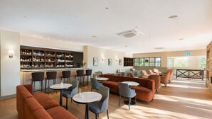 A bar area with a variety of seating options including sofas and round tables, a well-stocked bar with bottles, and a large window providing natural light. -  Peppers Clear Mountain (Cashmere)
