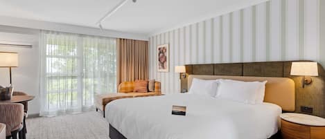 A hotel room with a large bed, a bedside table, a chair, a lamp, and a window with curtains.