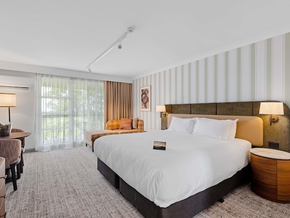A hotel room with a large bed, a bedside table, a chair, a lamp, and a window with curtains. - Peppers Clear Mountain (Cashmere)