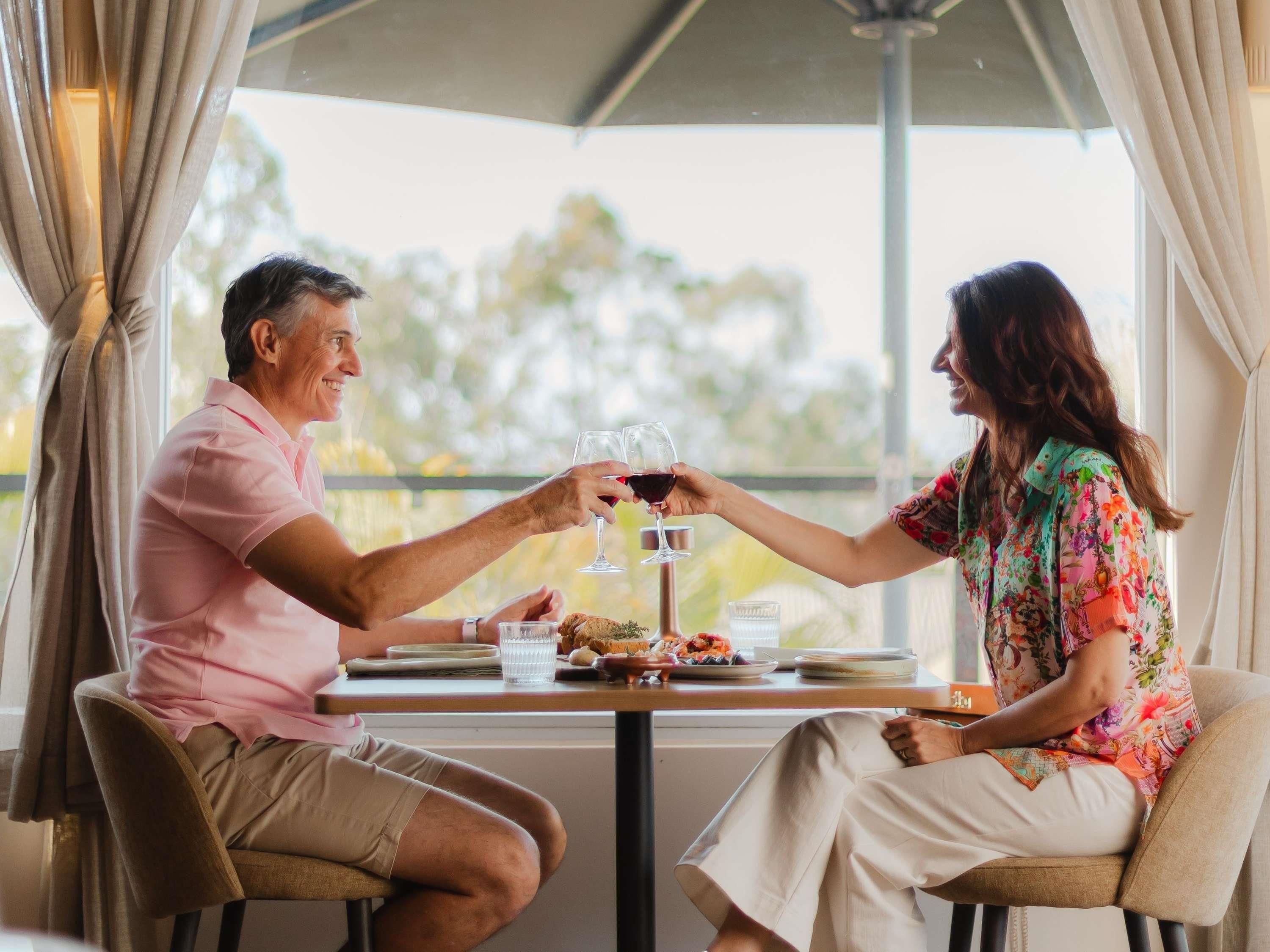 Two people seated at a table with a glass of red wine, a plate of food, and a glass of water.