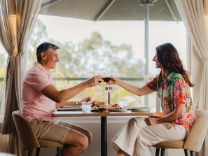 Dos personas sentadas a una mesa con una copa de vino tinto, un plato de comida y un vaso de agua.