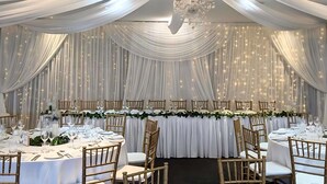 A banquet hall with round tables, white draped curtains, and a chandelier. - Mercure Clear Mountain Lodge (Cashmere)