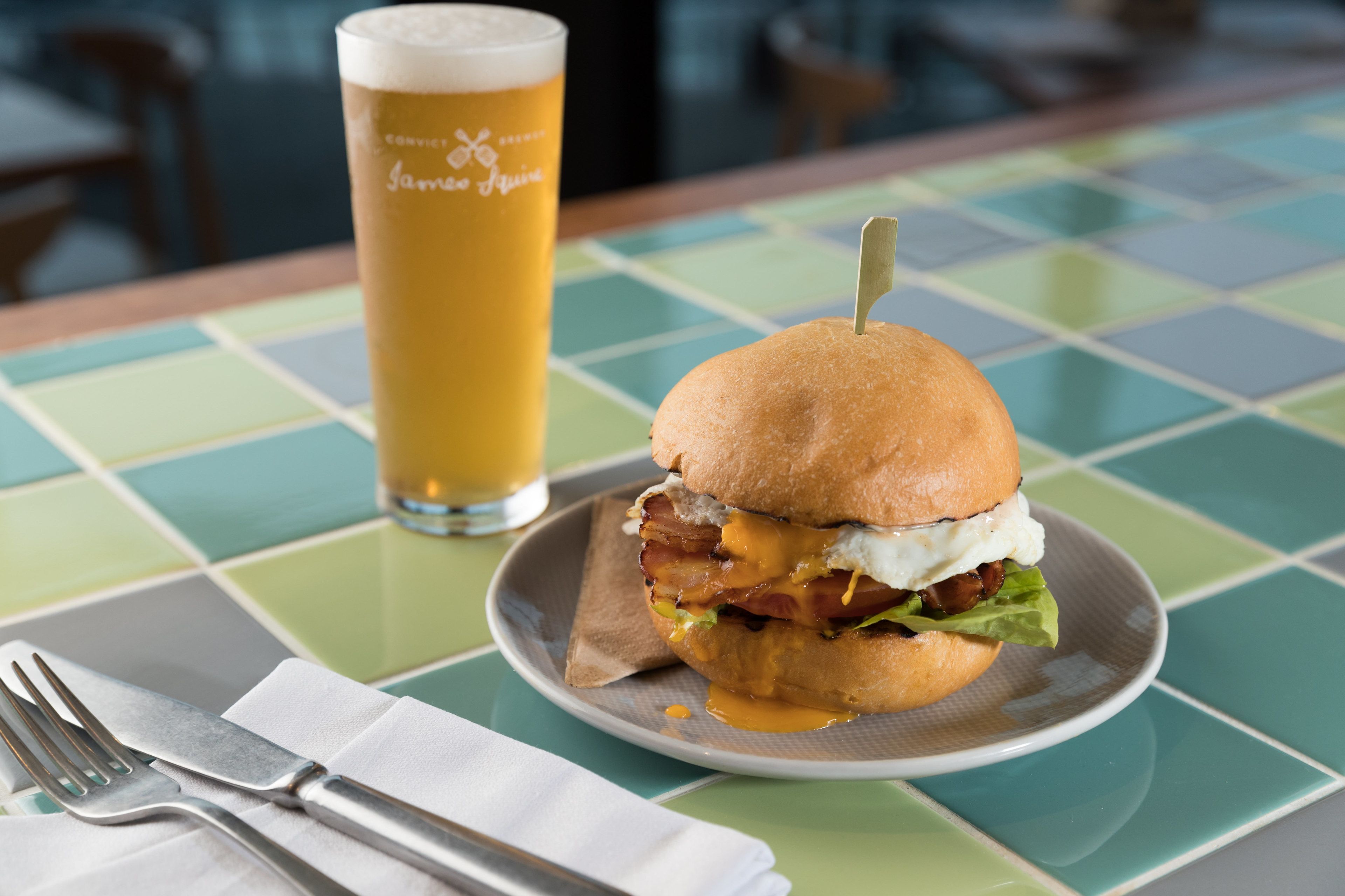 A meal with a burger and a glass of beer on a table with a checkered tablecloth.