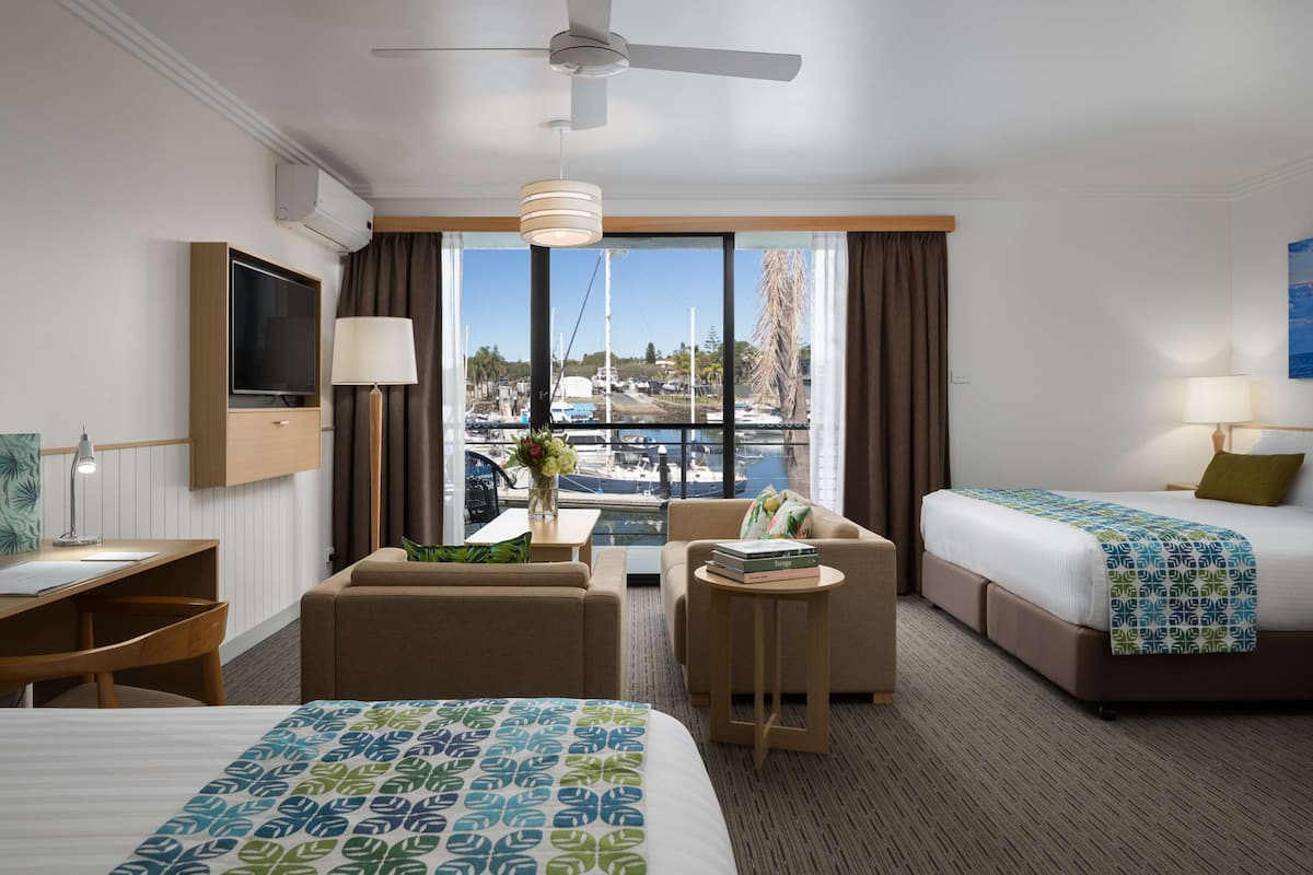 Une chambre d’hôtel avec deux lits, un bureau, une chaise, une petite table et une vue sur un port de plaisance.