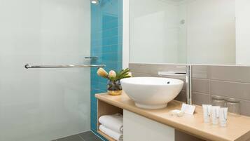 A modern bathroom with a large white sink, a glass shower enclosure, and a wooden vanity.