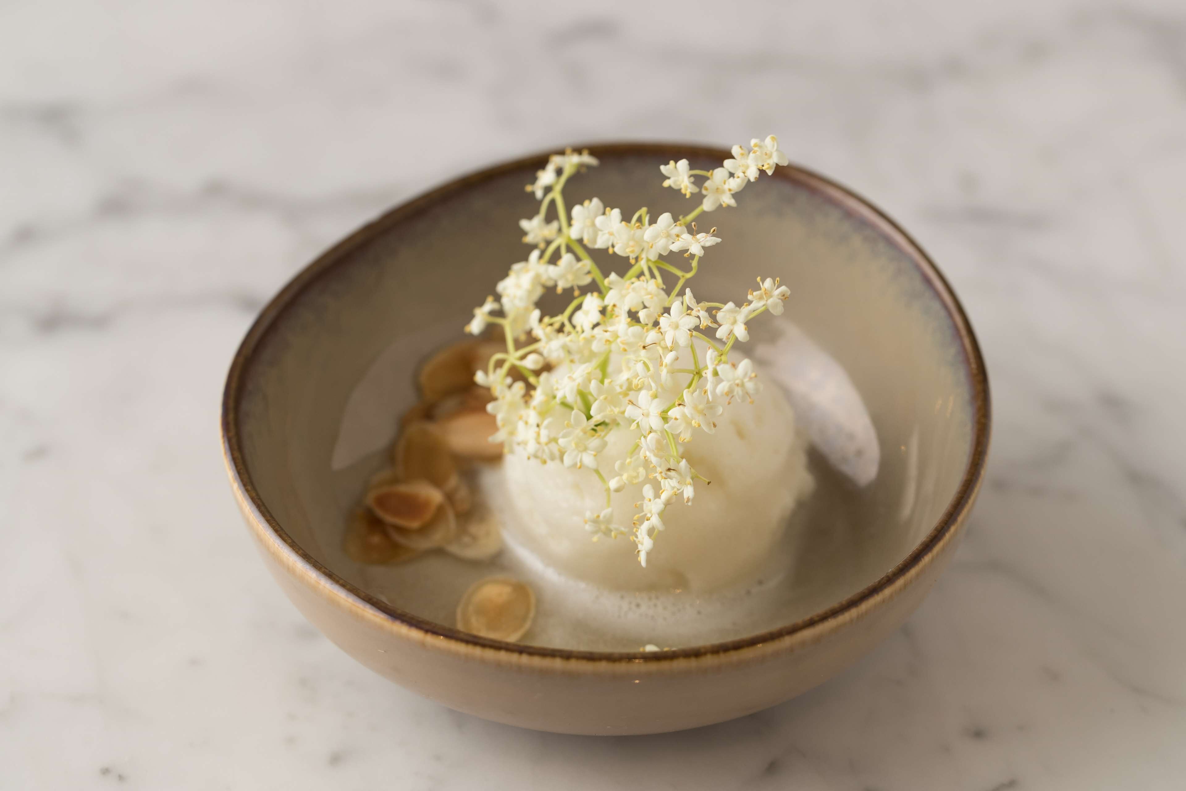A bowl of white food with a floral garnish on a marble surface.