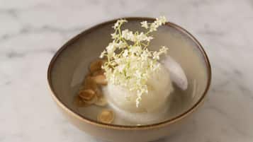 A bowl of white food with a floral garnish on a marble surface.
