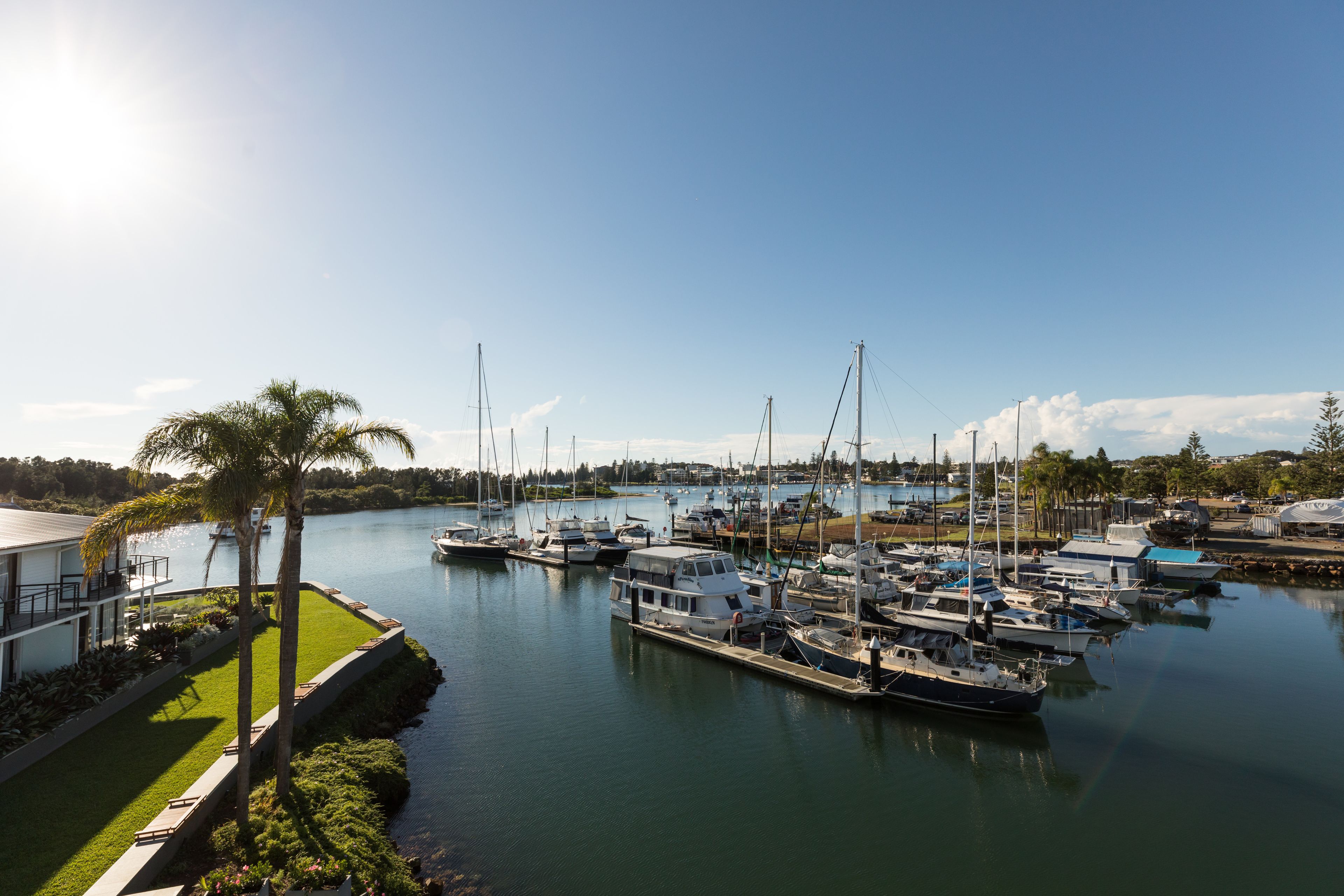 A marina with multiple boats docked, a well-maintained grassy area, and a clear sky.