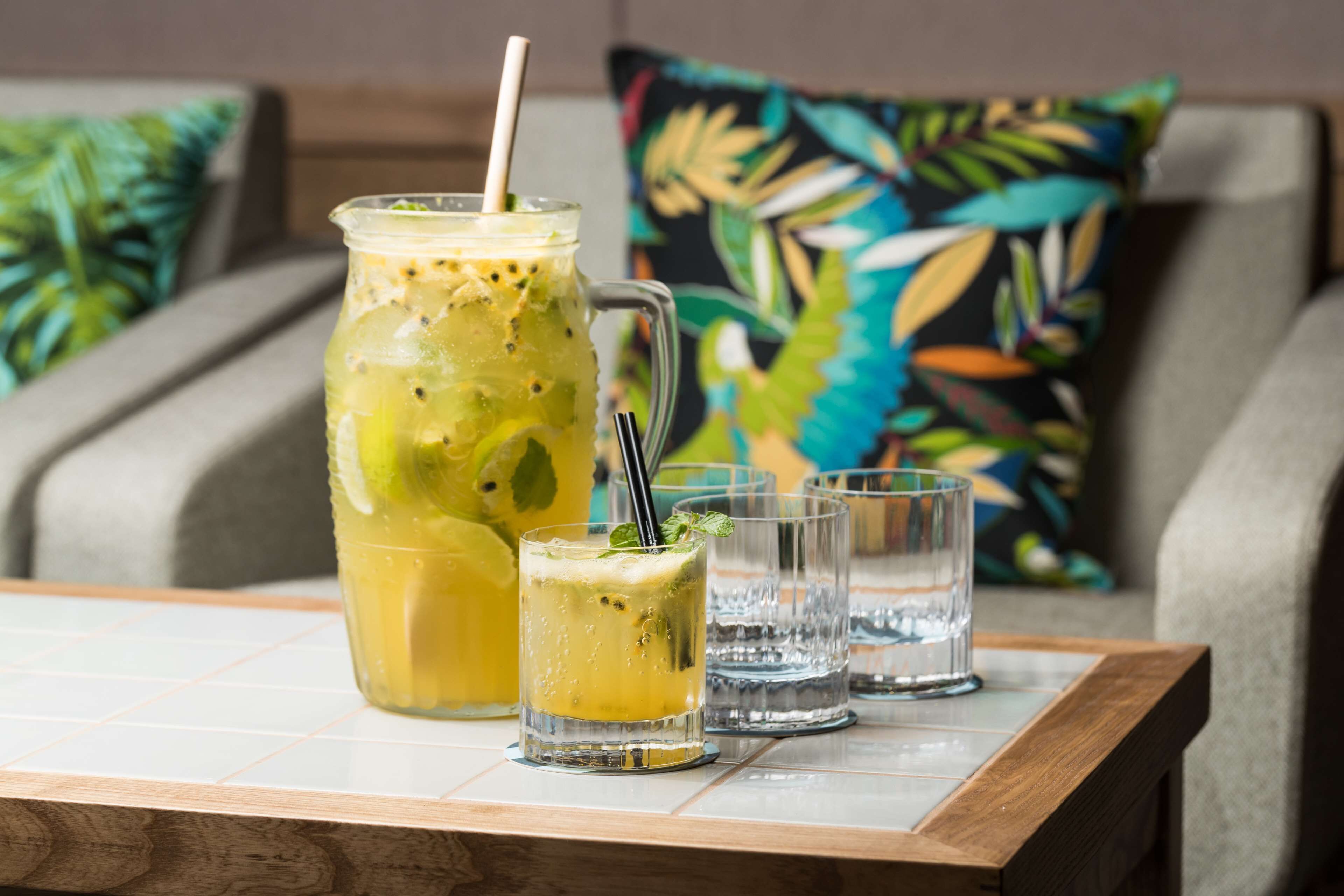 A glass of iced drink with a straw and mint garnish on a table, a mason jar with a similar drink, and two empty glasses.