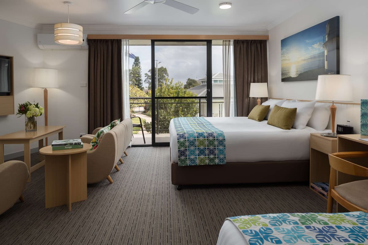 Une chambre d’hôtel avec un grand lit, un bureau, une chaise, une petite table et une vue sur l’extérieur.