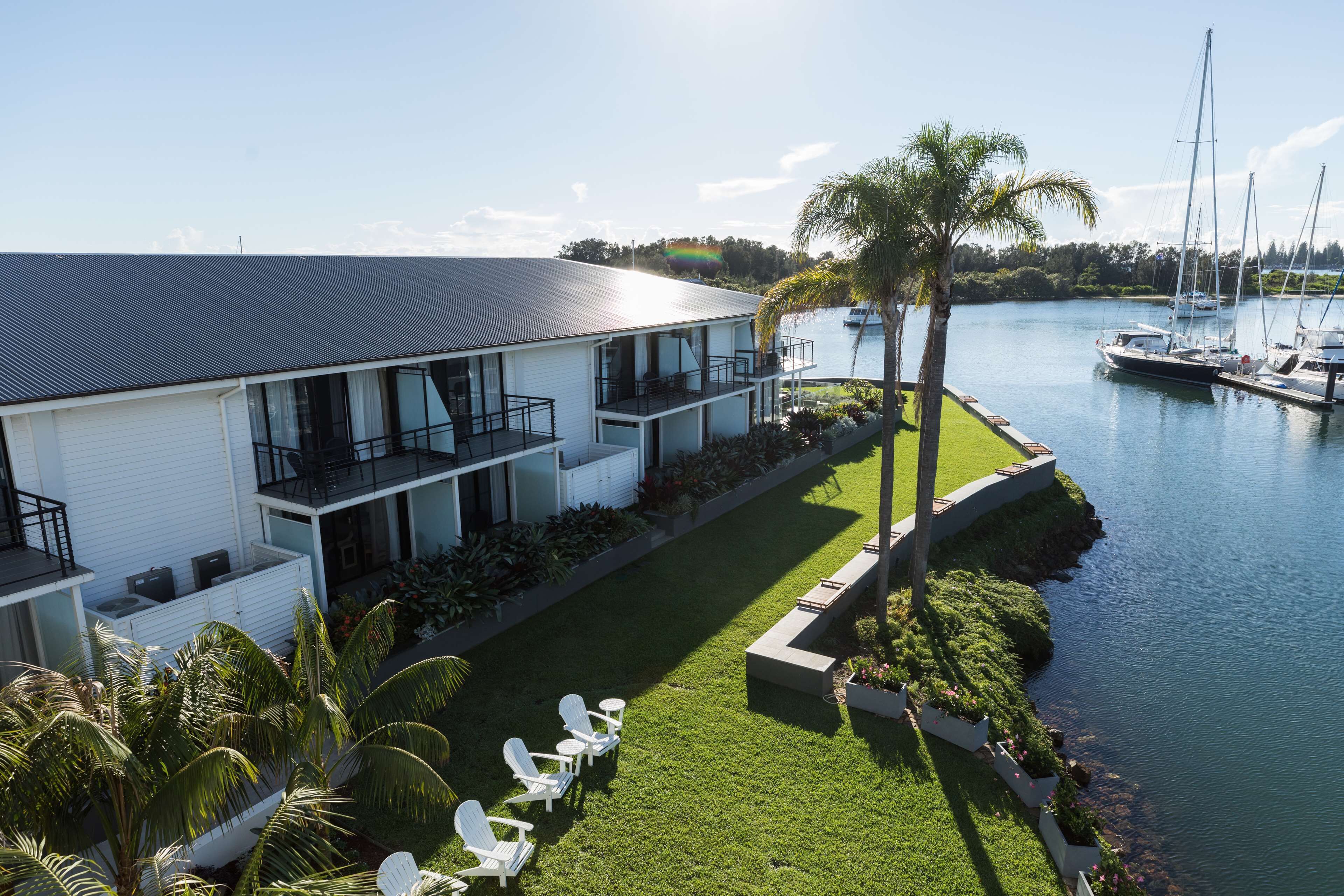 A modern two-story house with a balcony, a well-maintained lawn, and a marina with boats.