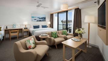Een hotelkamer met een bed, twee slaapbanken, een bureau, een televisie en een groot raam met uitzicht op zee.