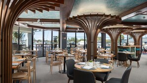 Un restaurant spacieux avec de hauts plafonds et de grandes fenêtres, offrant une vue sur le port de plaisance.