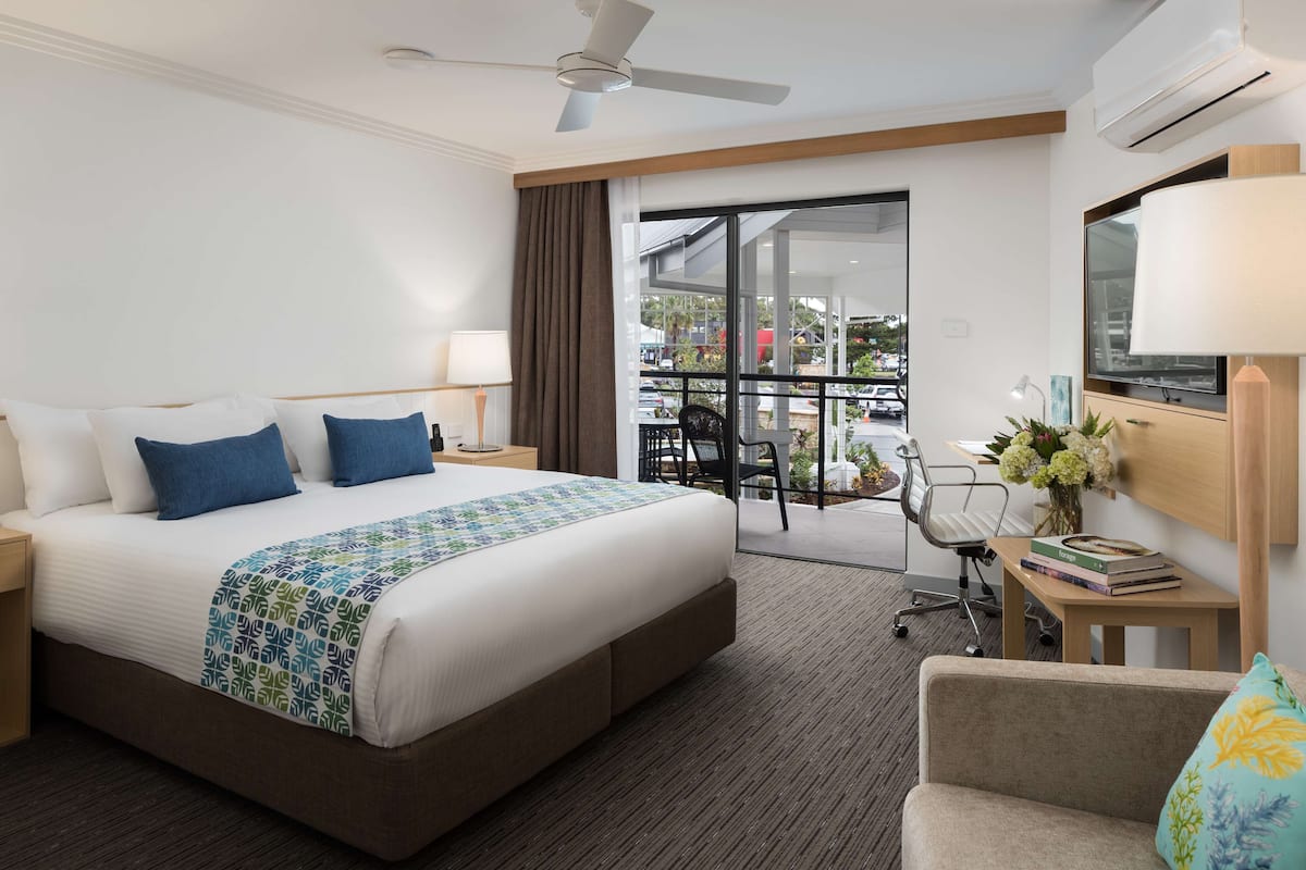 Une chambre d’hôtel avec un grand lit, un bureau avec une lampe, une chaise et une vue sur l’extérieur.