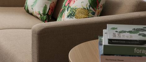 A beige sofa with floral pillows and a stack of books on a small wooden side table.