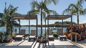 Un espace extérieur ensoleillé, aménagé avec deux pergolas couvertes, des fauteuils et une vue sur l’eau.