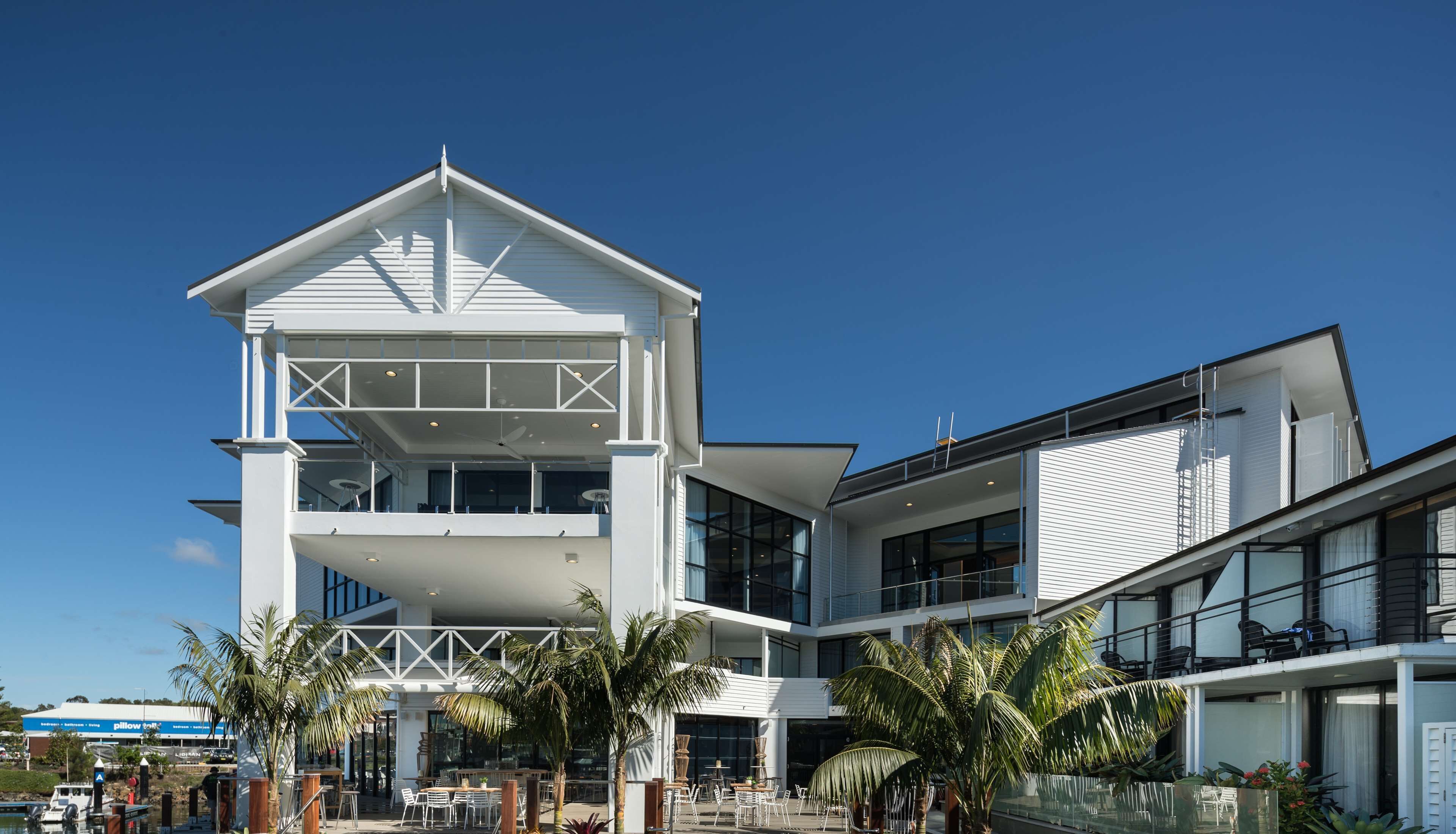 A modern two-story building with a prominent gable roof, large windows, and a covered outdoor seating area with tables and chairs.