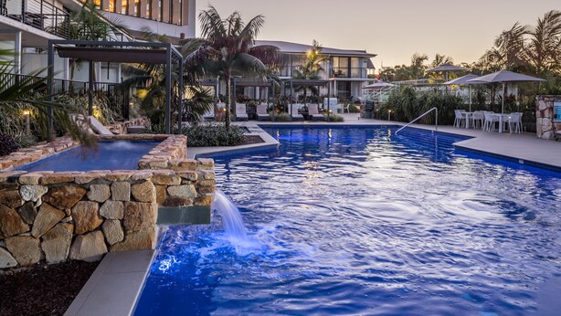 Un hôtel moderne doté d’une grande piscine extérieure, de murs en pierre et d’espaces de détente en plein air.
