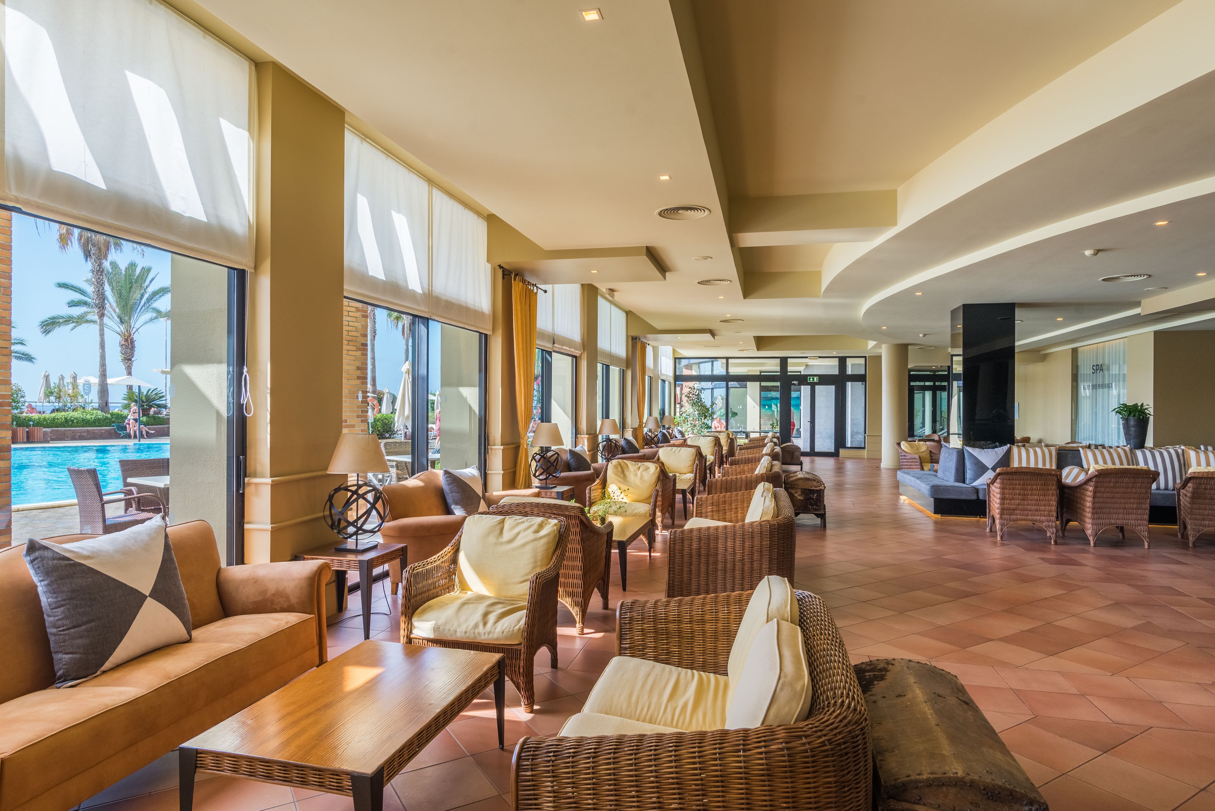 A spacious lobby with wicker furniture, large windows, and a pool view.