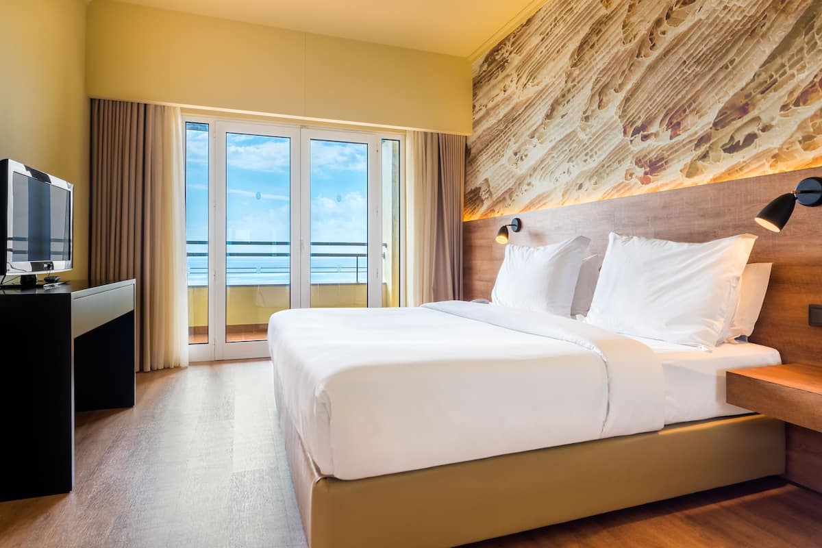 Habitació d'hotel amb un llit gran, escriptori amb televisió i vista a l'oceà a través d'una porta corredissa.