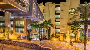 A multi-story hotel with a modern design, featuring a prominent entrance with glass doors, outdoor seating, and a stone facade.